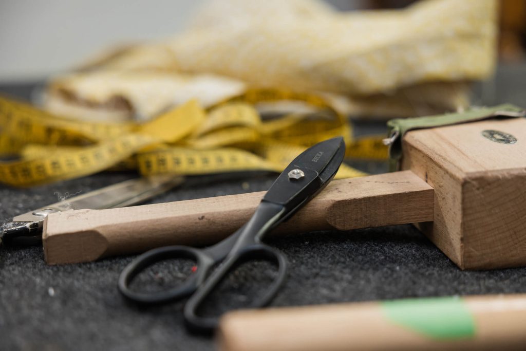 Set of upholstery tools, including a mallet, scissors, measuring tape and fabric on workshop bench