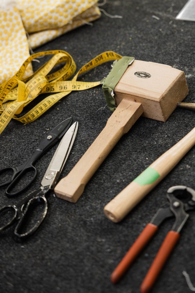 Set of upholstery tools, including a mallet, scissors, measuring tape and fabric on workshop bench